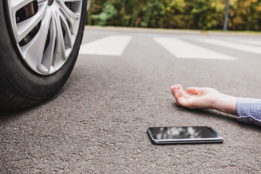 Pedestrian Accident Lawyer in Atlanta | Kaine Law A man’s cell phone lies next to him on the road, near a vehicle’s wheel.