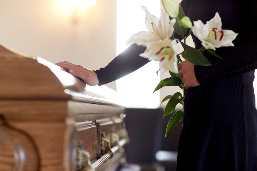 Wrongful Death Attorneys in Georgia | Free Consultations | 24/7 Support A woman holding white lilies places her hand on a casket